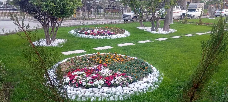 باغچه‌های گرد پر از گل فصلی با حاشیهٔ سنگ سفید و مسیر سنگ‌فرش روی چمن